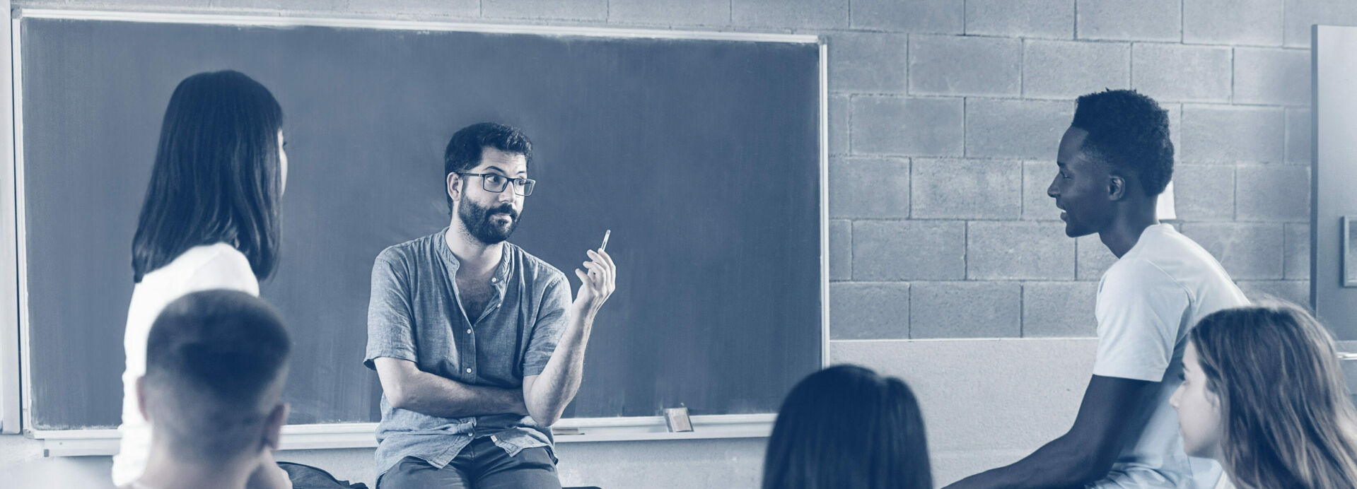 Teenaged students and bearded male teacher in group discussion in classroom