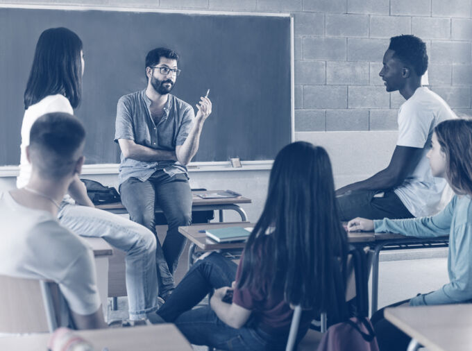 Teenaged students and bearded male teacher in group discussion in classroom